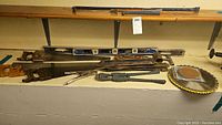 Multiple hand saws with wooden handles and metal blades, two spirit levels, crowbars, clamp, bolt cutters, pipe wrench, hand clamp tool, and circular saw blade.