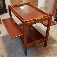 Front view of wooden folding beverage service table showing top tray, lower fixed tray, and expanded side shelves.