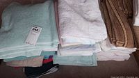 Photo showing neatly folded assortment of pastel, brown, and white towels in multiple sizes and types.