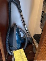 Kenmore canister vacuum with hose, wand, and floor nozzle, teal and gray colors, and a yellow dust bag packet on the floor.