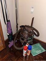 Overview of both vacuums with accessories and cleaning supplies on floor