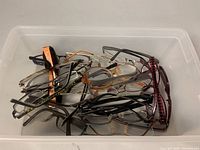 Over 12 assorted prescription glasses piled in a plastic bin, various frame styles and colors visible