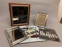 Shows metal album cover of The Beatles Anthology 1 next to two picture frames and a mirrored vanity tray