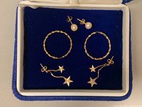 Two pairs of 14K gold earrings with studs and pendants, and one pair of textured 10K gold hoop earrings displayed in blue jewelry box.