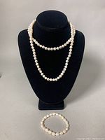 Full view of the baroque pearl lariat necklace displayed on a bust and matching stretch pearl bracelet placed below it.