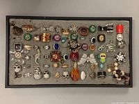 Full view of over 40 assorted costume rings arranged in a tray, showing a variety of designs, colors, and styles.