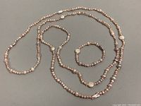 Full view of the 68-inch freshwater pearl lariat necklace coiled with the matching stretch bracelet beside it on a flat gray surface.