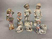 Photo showing all seven bisque figurines including children and poodles arranged in a row on a flat surface, showcasing size and details