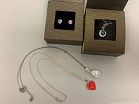 View of two silver necklaces with pendants and stud earrings displayed in jewelry boxes