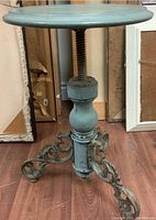 Side view showing the round wooden seat, adjustable screw column, and ornate cast iron legs with paint wear and some rust.