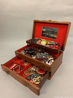 Full view of the open wooden jewelry box with multiple compartments filled with assorted costume jewelry pieces including bracelets, necklaces, and bangles.