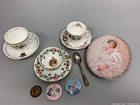 All items displayed together showing teacups, saucers, commemorative pins, medallion, and Diana plate