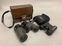 Bushnell and Olympus binoculars with their respective carrying cases displayed on a table.