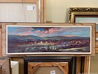 Full front view of a framed horizontal landscape oil painting with broad panoramic cityscape and natural elements.