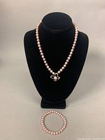 Necklace displayed on black bust stand with the matching stretch pearl bracelet placed below it.