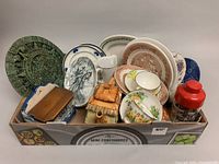 Full box view showing assorted chinaware including Aztec calendar plaque, cottage style teapot set, assorted plates, and small wooden box.