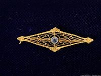 Front close-up of vintage 14K gold filigree brooch with central round sapphire gemstone on dark fabric background showing detailed gold design and gemstone color.