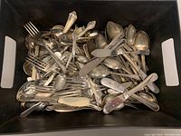 Black bin filled with assorted vintage cutlery pieces including forks, knives and spoons