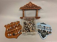 Container of assorted loose souvenir and collector spoons along with three wooden wall display stands, one carved and two crest-shaped