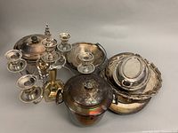Multiple pieces of vintage silver plated servingware including candelabras, ice buckets, and trays, arranged together showing tarnish and patina.