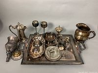 Wide shot showing the full set of silver plated servingware on a flat surface including tray, pitcher, bowls, candleholders, and goblets.