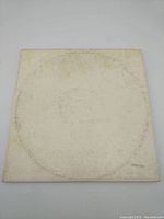 Front of white album cover showing overall staining and discoloration with faint embossed Beatles text and stamp number.