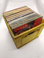 Yellow plastic crate filled with vinyl records standing upright, showing Queen Sheer Heart Attack album