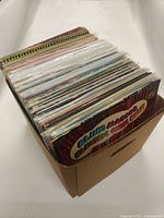 Photo showing a cardboard box filled with numerous vinyl records with visible colorful album covers.