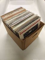 Box containing approximately 30 vinyl records upright in sleeves, showing mostly the spines and some front covers.