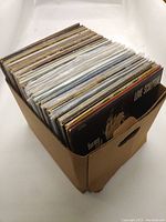 Side view of cardboard box filled with over 70 vinyl records showing album spines and some covers visible