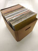 Photo of a densely packed cardboard box filled with vinyl records showing the variety and quantity.