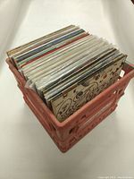 Photo showing a plastic crate holding a collection of vinyl records in sleeves, standing upright.
