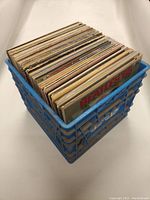 Blue plastic crate filled with numerous 12-inch vinyl records, viewed from above and side.