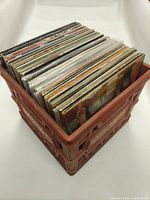 Photo of approximately 40 vinyl records stored upright in a red plastic milk crate, albums are visible from top down
