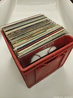 Photo of red plastic crate filled with vinyl records, showing Queen's Greatest Hits album cover in front.