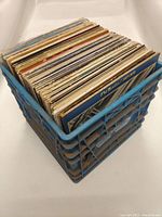Blue plastic crate filled with approximately 40 vinyl records shown standing upright to reveal edges and thickness of album covers.