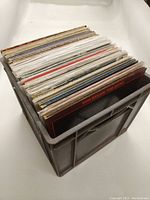 Photo of plastic crate filled with approximately thirty 12-inch vinyl records, organized side vertically showing visible spines and album covers on the edges.