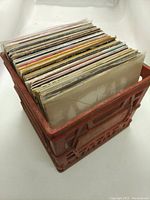 Plastic red milk crate filled with vinyl record sleeves viewed from above