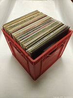 Red plastic crate filled with numerous 12" vinyl records, arranged vertically.