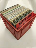 Photo of red plastic crate filled with vinyl records, mostly 12" size, showing 'Never Mind The Bollocks' album cover at front