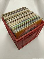 Red plastic crate filled with about 30 vinyl records showing a side view.
