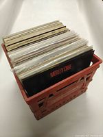 Red plastic crate filled with vinyl records, showing record spines and one visible Mötley Crüe album cover