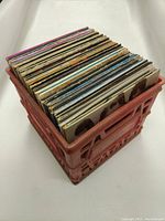 Red plastic crate containing approximately 30 vinyl records.