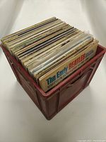 Plastic storage crate filled with approximately 40-50 vinyl records seen from an angle.
