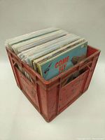 View of the red plastic Coca-Cola crate filled with vinyl records standing upright.