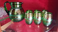 Photo shows the pitcher and six matching green crystal glasses with gold bands on a mirrored shelf.