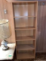 Front-facing image of the 5 tier wooden bookshelf showing all shelves and structure with light wood finish, photographed next to wall and lamp.