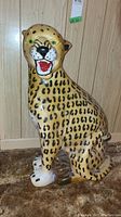 Front view of seated ceramic leopard statue showing painted face, open mouth and front paws