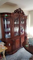 Front view of ornate wooden china cabinet showing glass display area and wood base with storage.