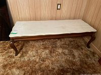 Full view of the coffee table showing the white stone top and scalloped edges with carved wooden legs on a brown carpeted floor.